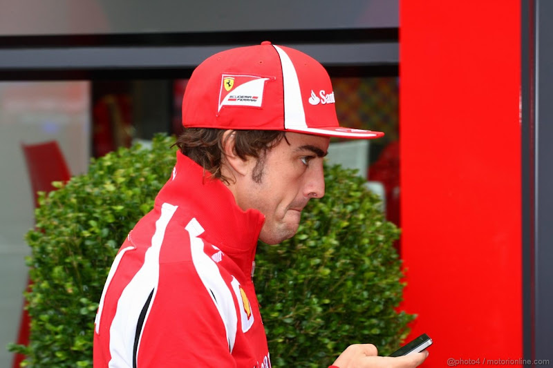 Фернандо Алонсо с телефоном проходит мимо зеленого куста у паддока Ferrari на Гран-при Венгрии 2011