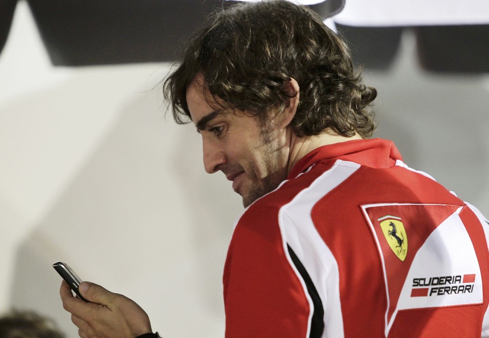 улыбающийся Фернандо Алонсо смотрит в телефон на Гран-при Сингапура 2011