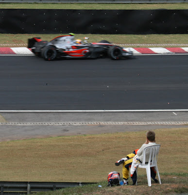 Хейкки Ковалайнен на пластиковом кресле смотрит на проезжающего Льюиса Хэмилтона на McLaren на Гран-при Бразилии 2007