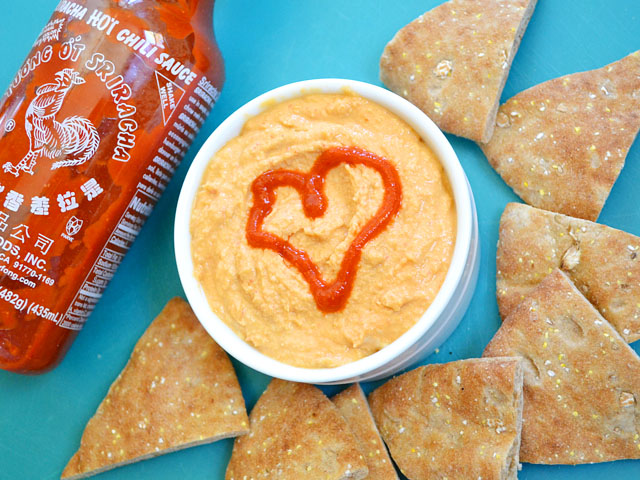 Bowl of Sriracha Hummus with heart made out of Sriracha - pita chips on the side with bottle of Siracha 