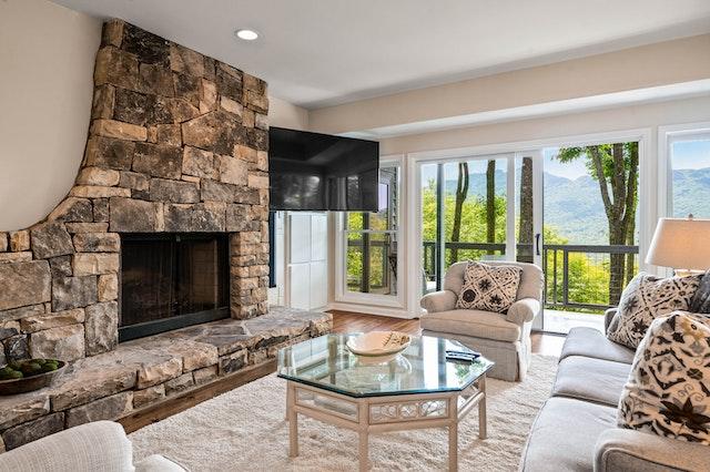 A living room in a luxury home with a stone fire place, glass coffee table and a large window