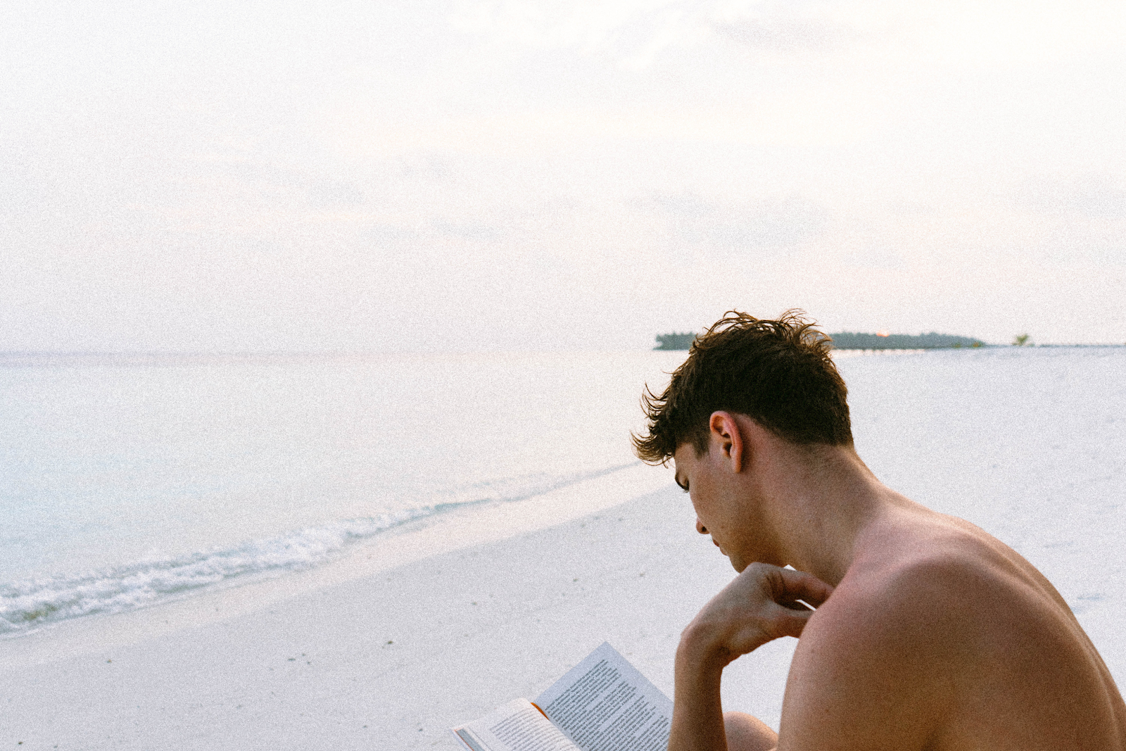 A man reading a book while on the beach.