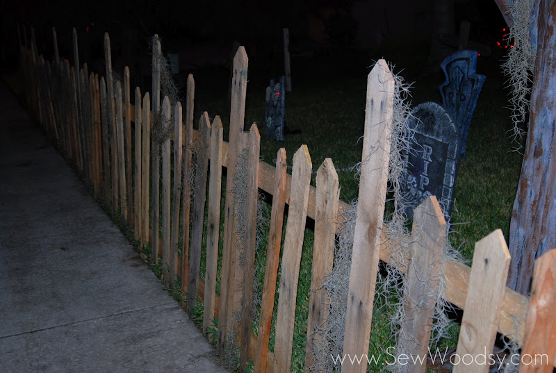 Wood pallet fence with moss and graveyard in background at night.