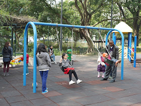 adults watching kids on a swing set at the King George V Memorial Park in Kowloon, Hong Kong