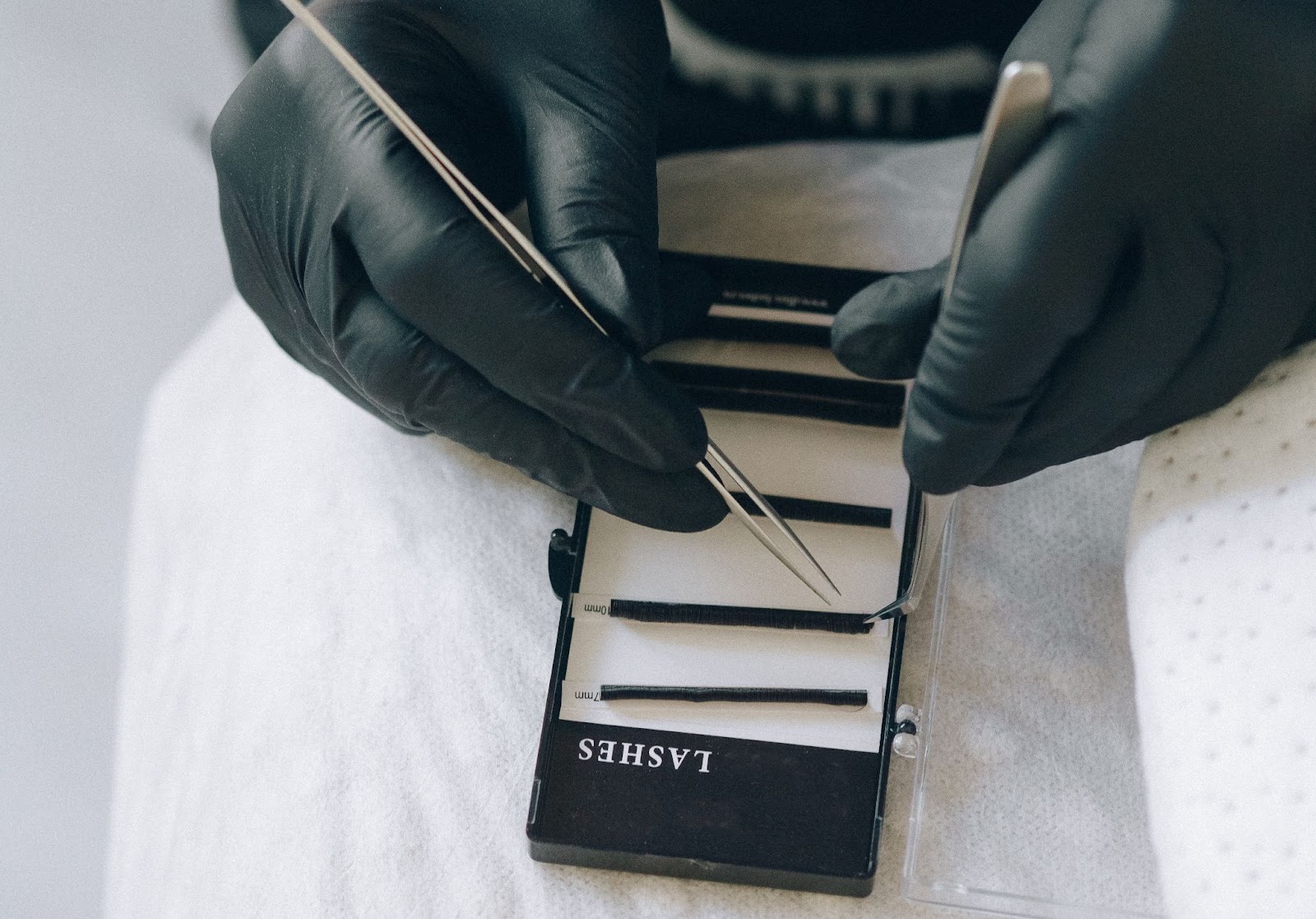 A lash technician wearing gloves picks out individual lashes from a pack of extensions