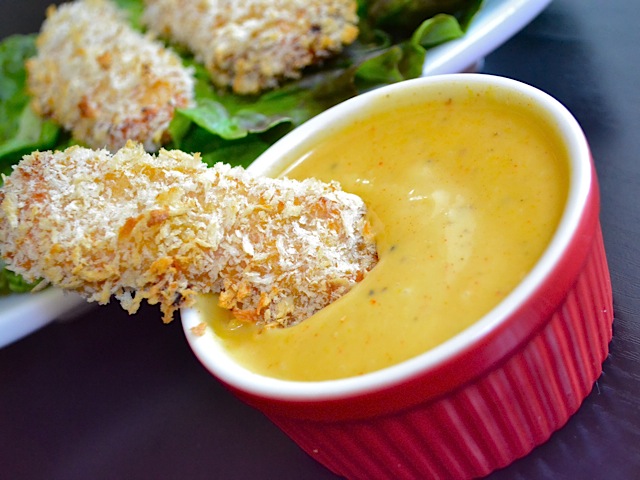 One honey mustard chicken strip being dipped into sauce 