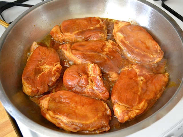 marinated raw pork chops placed in skillet on stove top 