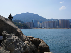 man sitting on a rock and looking across the water at Lei Yue Mun, Hong Kong