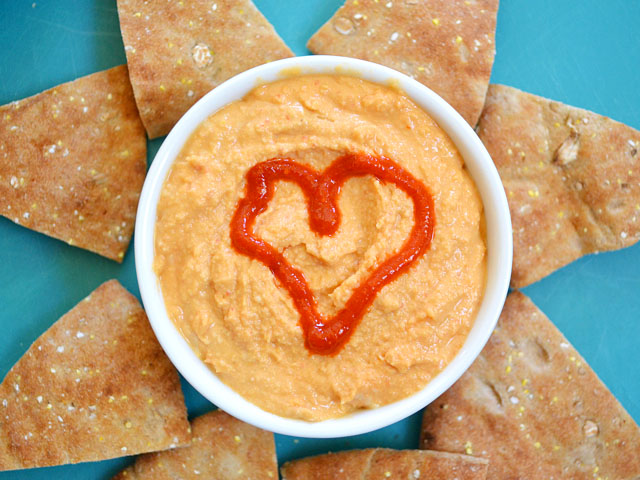 Bowl of Sriracha Hummus with heart made out of siracha - pita chips in circle around bowl 