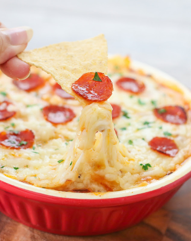 photo of a chip being dipped into a 7 Layer Pizza Dip