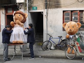 two men altering a wedding dress for a large stuffed bear with the groom stuffed bear nearby