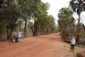 three people riding a motorbike on a dirt road