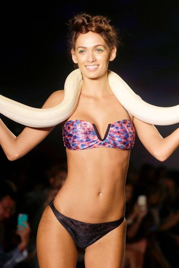 A model walks down the runway with a live snake wearing swimwear designed by We Are Handsome during the Mercedes-Benz Fashion Week Swim show, Friday, July 18, 2014, in Miami Beach, Florida.