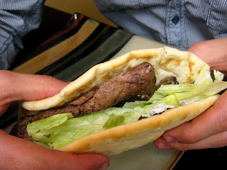 A hand holding a beef gyro in a pita with lettuce.