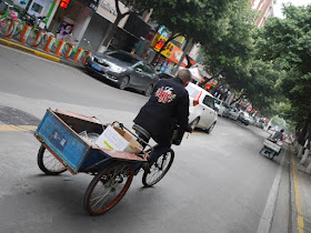 man wearing a Looney Tunes jacket riding a tricycle cart