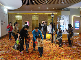 adults and children enjoying fake autumn leaves at a mall