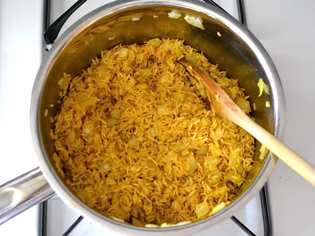 toasted rice in pot being stirred with wooden spoon 