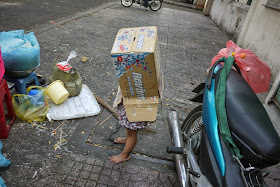 a barefoot girl with a with box over the top of her body playing on a a sidewalk in Ho Chi Minh City, Vietnam