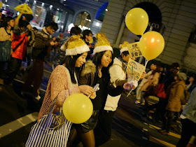 young women wearing yellowish Santa hats and carrying Umbrella Movement materials