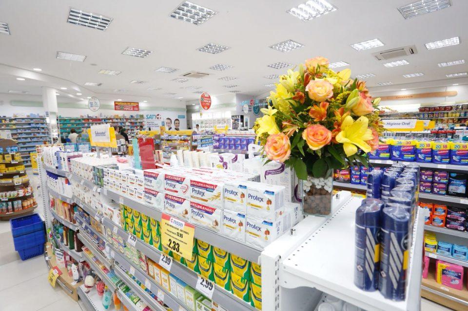 A imagem mostra uma gôndola de farmácia com um vaso de flores em cima. Detalhe que pode ser interessante quando se pensa em como organizar uma farmácia.