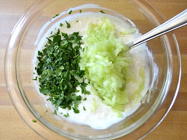 cucumber and cilantro added to yogurt mixture in mixing bowl 