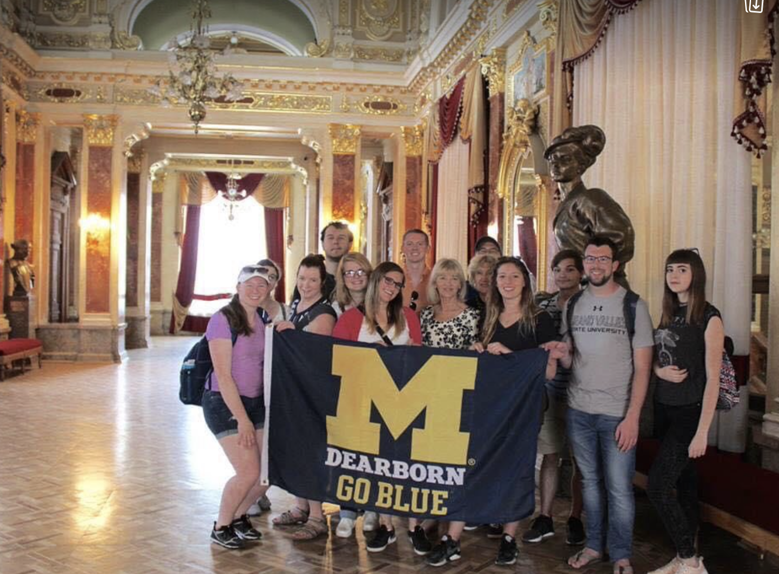 Group of students holding a UM-Dearborn flag in the lobby of a historic building