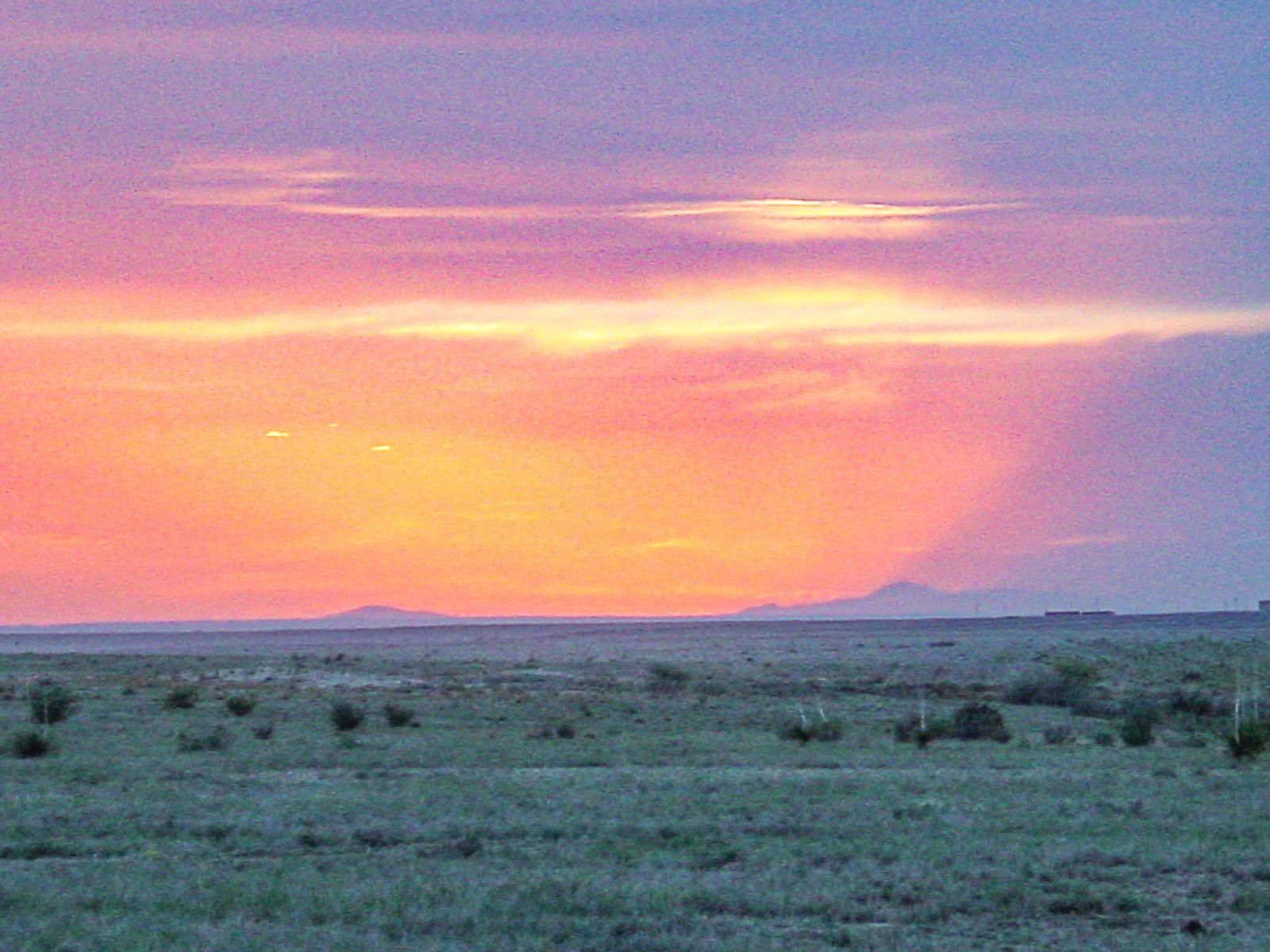 A purple and orange sunset over distant mountains and desert foreground. 