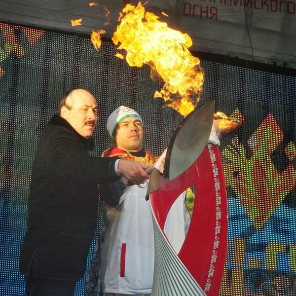 The leader of Dagestan Ramazan Abdulatipov, left, and an unidentified Olympic torch bearer light an Olympic flame during an Olympic torch relay in the city of Makhachkala, regional capital of southern Russian Caucasus province of Dagestan.