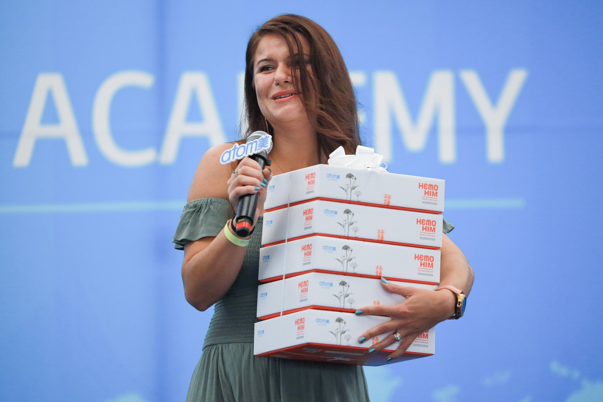 A person holding a microphone and a stack of boxes

Description automatically generated