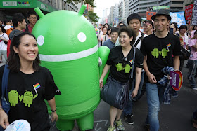 Person in an Android Robot suit and others wearing shits with two Android Robots holding hands and a rainbow flag