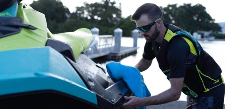 A man in sunglasses and safety vest changing the oil on his personal watercraft for the winter off-season. 