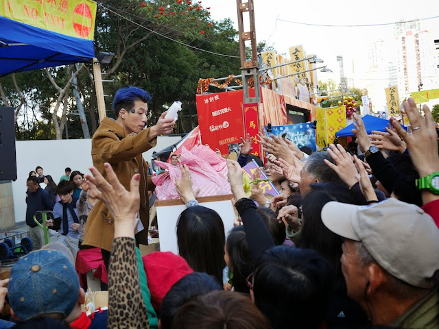 man with blue dyed hair holding an item while many people in a crowd reach out their hands