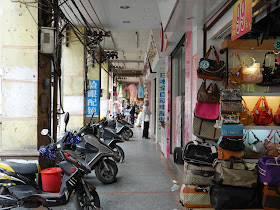 buildings overhanging a sidewalk with motorbikes and bags for sale in Yangjiang, China