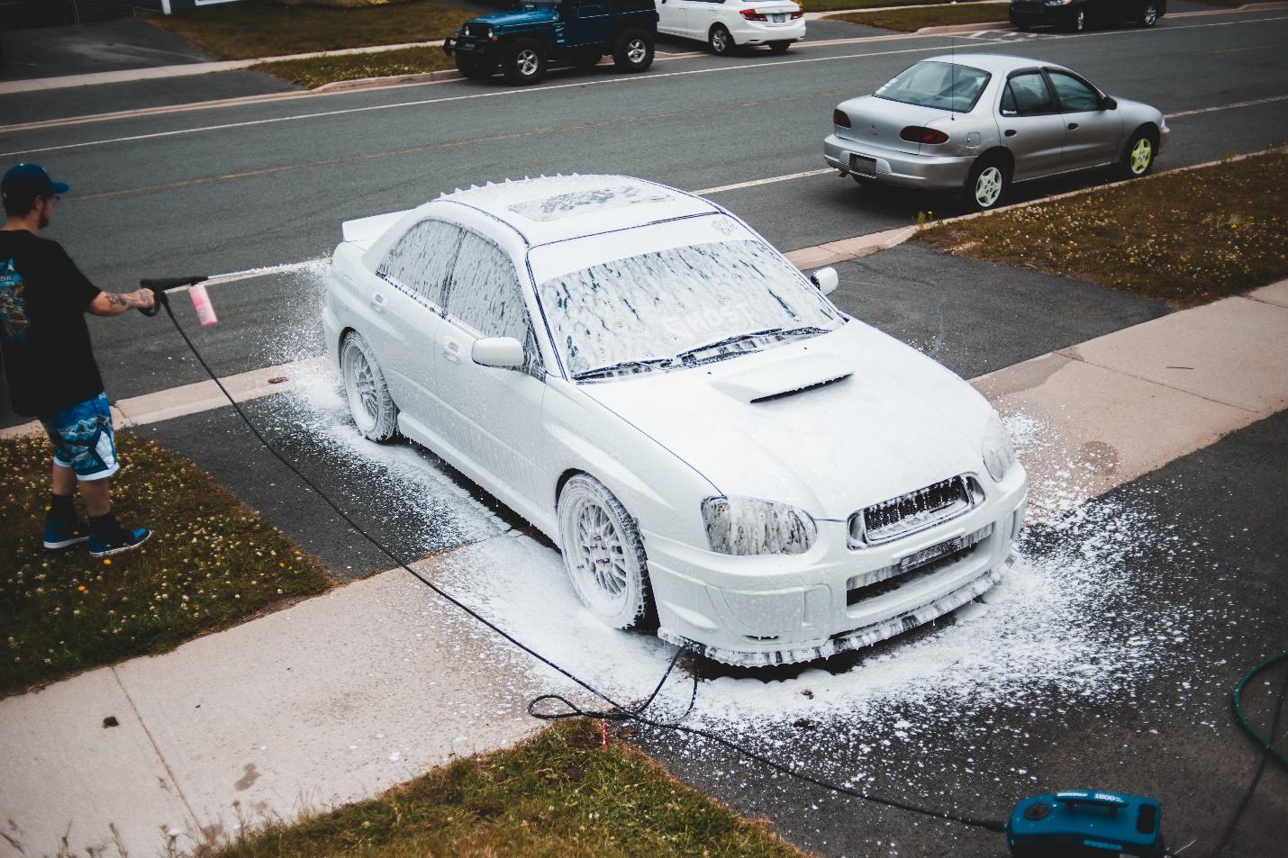 A person sprays foam using a pressure washer on a Subaru in a DIY Car Wash.
