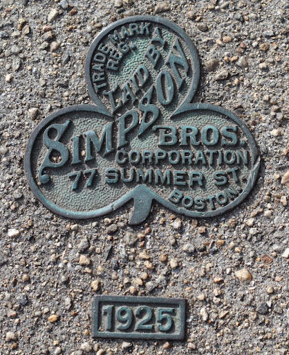 clover-shaped metal plaque embedded in a sidewalk, with information about the firm which poured the concrete in 1925