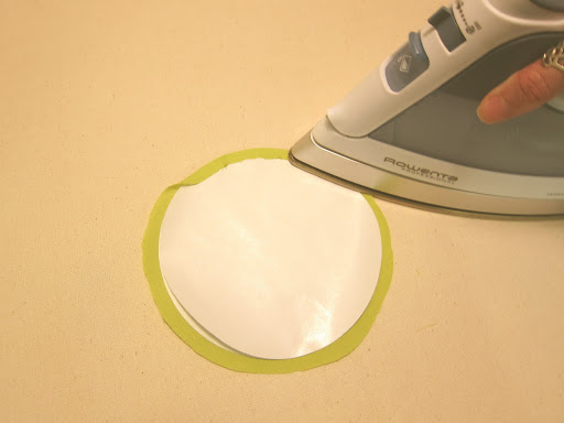 Fold the excess fabric over the two paper circles, and press in place (the fabric will stick to the top circle). If a bump shows up, simply lift the fabric and press again - freezer paper allows repositioning. Fold the excess fabric over the two paper circles, and press in place (the fabric will stick to the top circle). If a bump shows up, simply lift the fabric and press again - freezer paper allows repositioning.