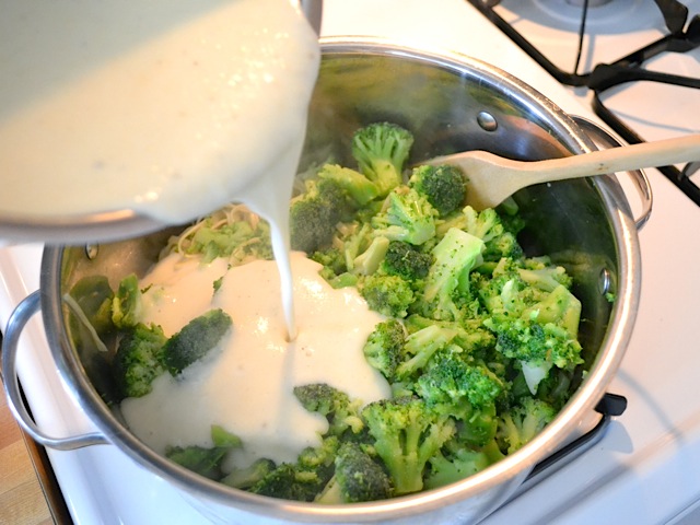 broccoli and cooked pasta in pan with sauce being poured over 