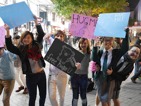 high school girls excitedly holding signs reading 'Hug Me' and "free hugz'