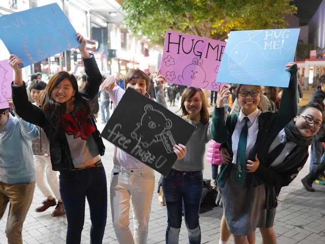 high school girls excitedly holding signs reading 'Hug Me' and "free hugz'