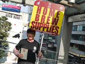man wearing HK Brewcraft shirt holding sign reading "Home Brew Supplies"