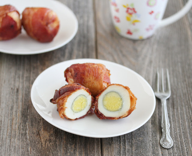 two Baked Bacon Wrapped Eggs on a plate with one sliced in half