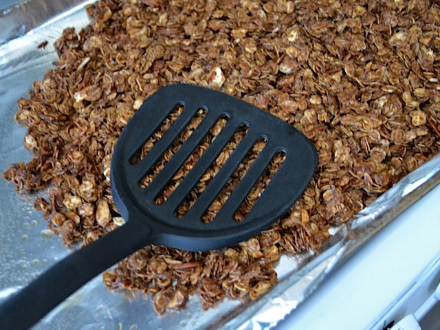 baked granola with spatula to scoop off baking sheet 