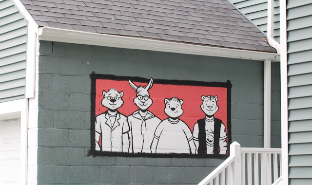a mural on the side of a garage, of four people depicted with the heads of cartoon animals