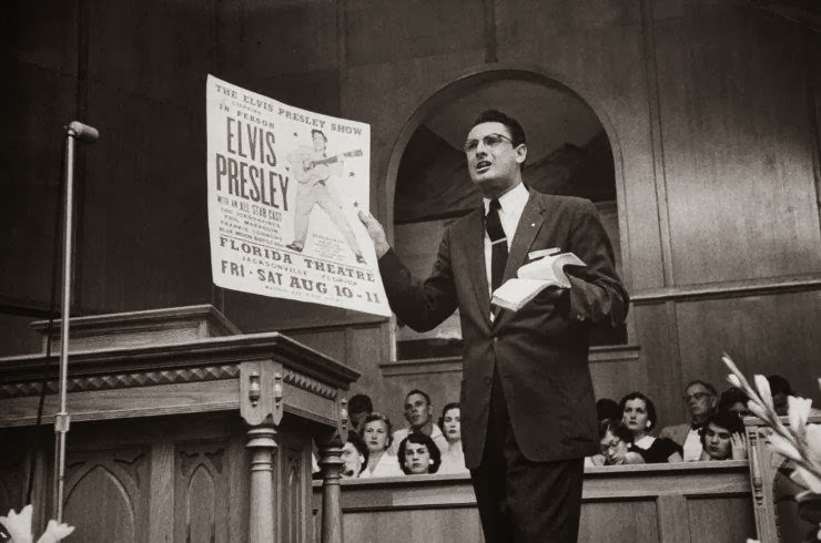 O pastor Robert Gray faz uma comparação em seu púlpito entre um cartaz de Elvis e a Bíblia, provavelmente destacando que o comportamento, dança e som do cantor não era algo aconselhável para os princípios cristãos. (Foto: Robert W. Kelly – Time & Life/Getty Images)
