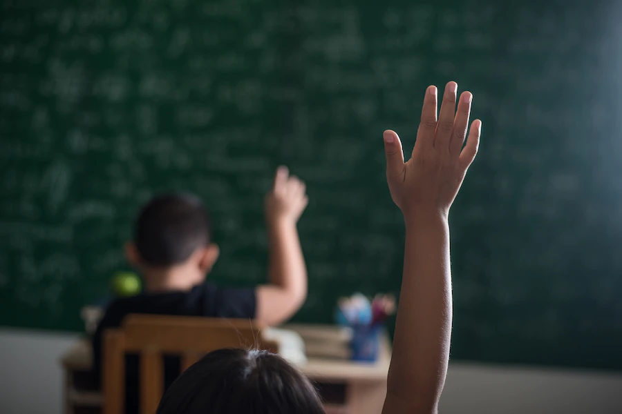 Gestão escolar para escolas públicas: criança levantando a mão em sala de aula
