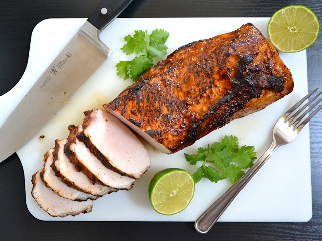 Sliced chili lime pork loin on cutting board with knife and fork 