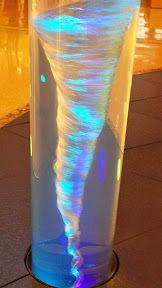 A fun water funnel art installation inside Crystals as I walk towards Aria in Las Vegas. There is something at the bottom which spins the water and colored lights that the water tornado will pick up