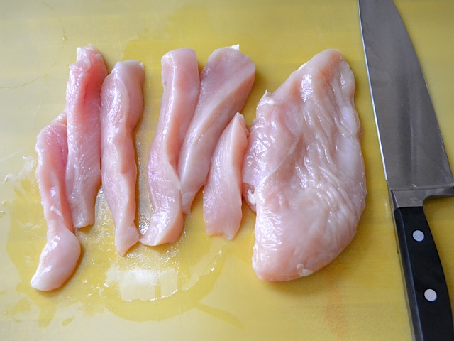 chicken being sliced into strips with a knife 