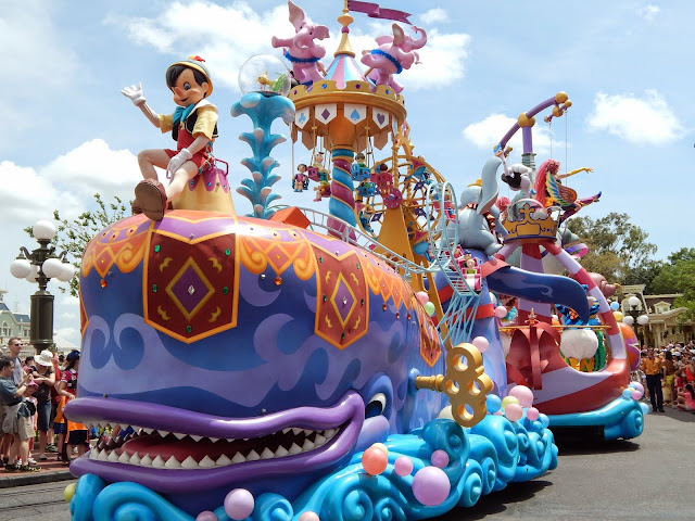 New Disney World Parade: Festival of Fantasy. Next comes Pinocchio, riding a wind-up whale. In the back Dumbo flaps his ears. A rollercoaster winds around the float as a Ferris wheel turns. 