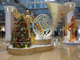 large angel playing a large French Horn next to a Christmas tree